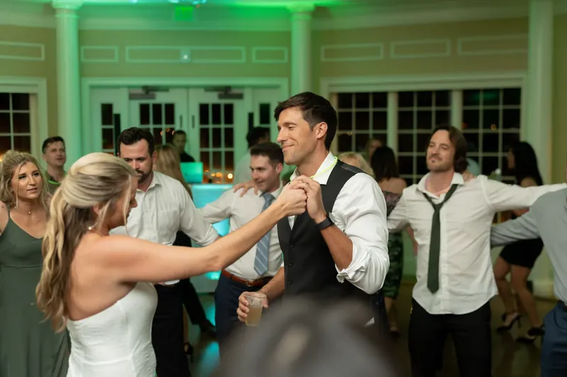 Landon dances with a guest in a white sleeveless dress under green ambient lighting.