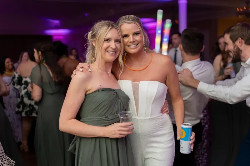 Two women in formal attire embrace and smile together during the evening celebration.
