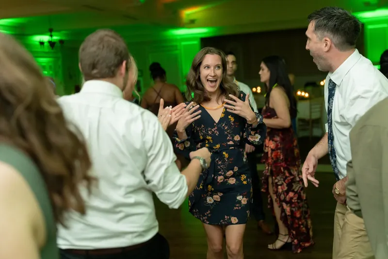 Guests dance under green lighting at River House Events, with a woman in a black floral dress laughing in the center.