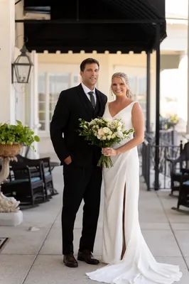 The couple walks hand in hand across the patio in black and white attire, Kimberly's train trailing behind.