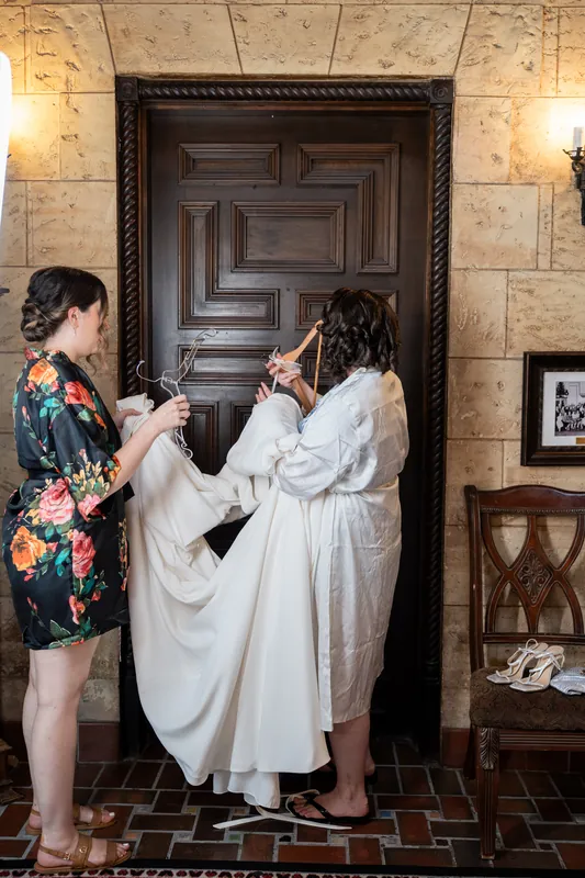 A person in a floral shirt helps adjust the white gown of someone getting ready at The Treasury on the Plaza, St. Augustine.