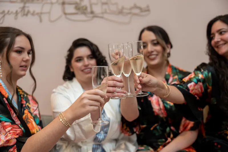A group of five people raise champagne glasses in a celebratory toast at The Treasury on the Plaza, wearing coordinating robes.