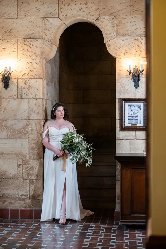 Someone in an off-shoulder white gown holds a cascading greenery bouquet beneath an arched doorway at The Treasury.