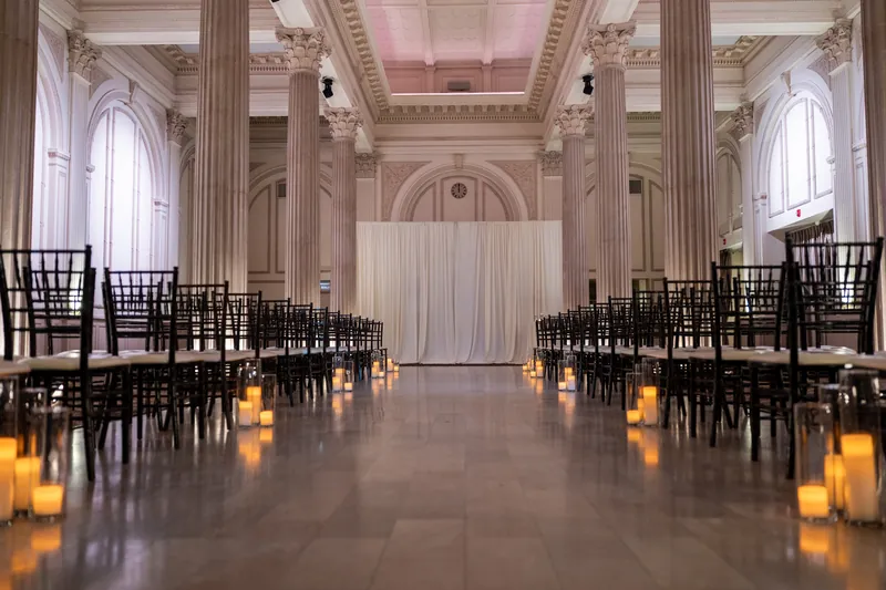 The Treasury's grand ceremony hall stretches ahead with black chiavari chairs lining a center aisle, lit candles glowing beneath a coffered ceiling.