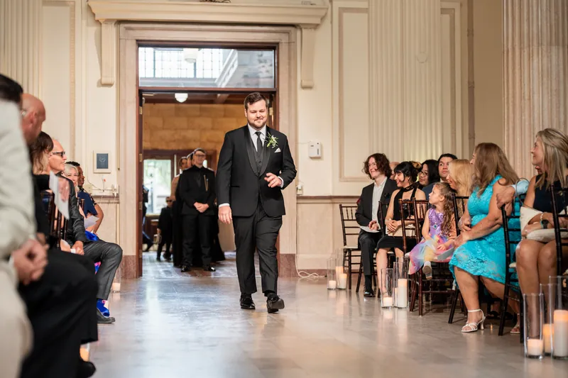 A person in a dark suit walks through The Treasury on the Plaza's classical interior with cream columns and arched doorways.