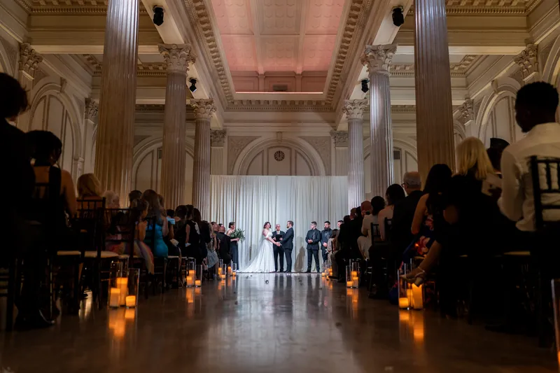 Candlelit rows line the ceremonial aisle in The Treasury's neoclassical hall, guests seated on either side.