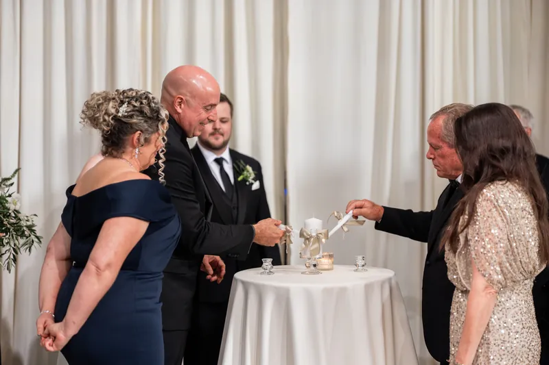 A man in a dark suit converses with two women near a cocktail table draped in white fabric.