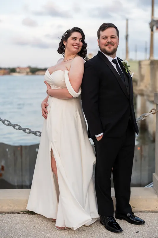 Kimberly and Ty pose together at the waterfront railing, with the bay and distant shoreline visible behind them.