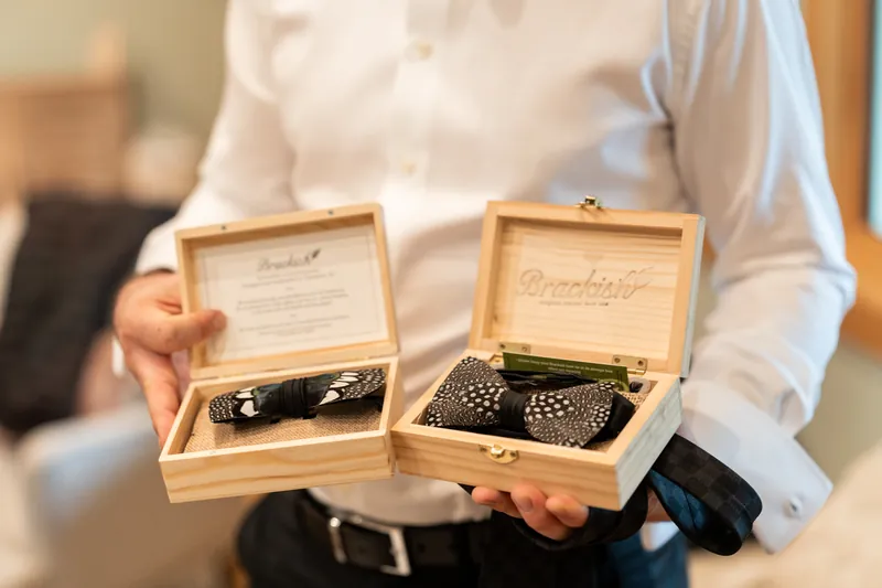 Feather bow ties in wooden Brackish boxes held by groom