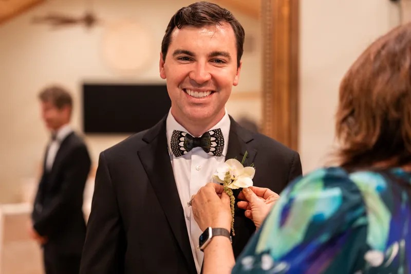 Groom smiling while getting orchid boutonniere pinned on his lapel