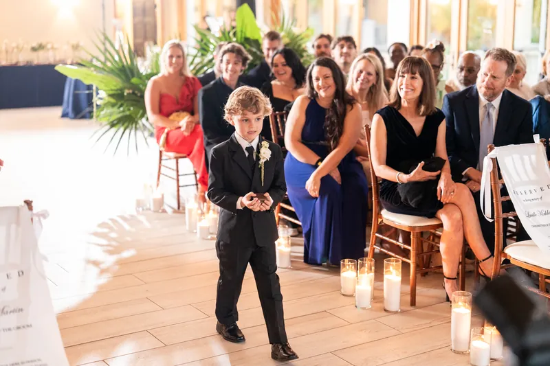 Ring bearer walking down the aisle as guests smile and watch