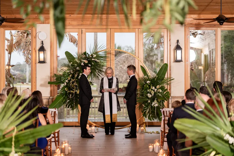 Ceremony at the gold arch with officiant reading, tropical greenery, and candlelight