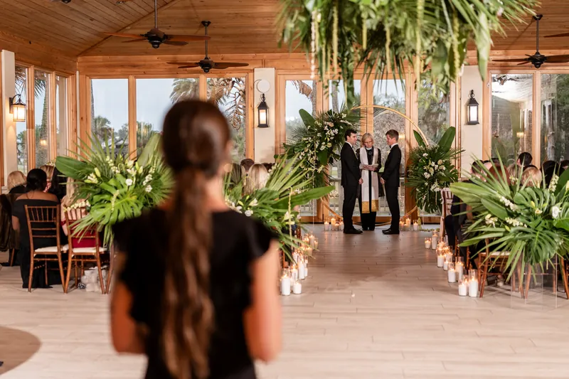 View down the aisle during the ceremony with tropical greenery and woman watching