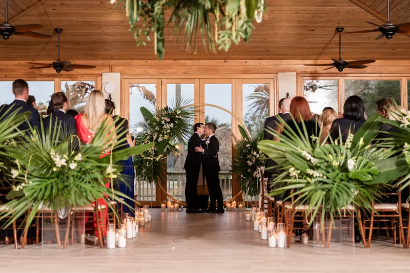 Austin and Kirkland sharing their first kiss at the altar under the gold arch with tropical greenery