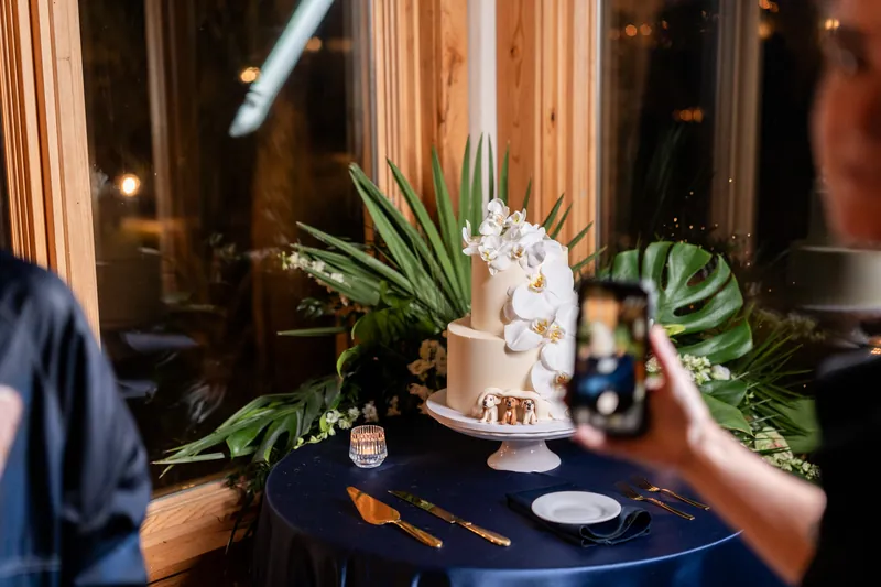 Wedding cake with orchids and fondant dog figurines peeking from the base surrounded by tropical greenery