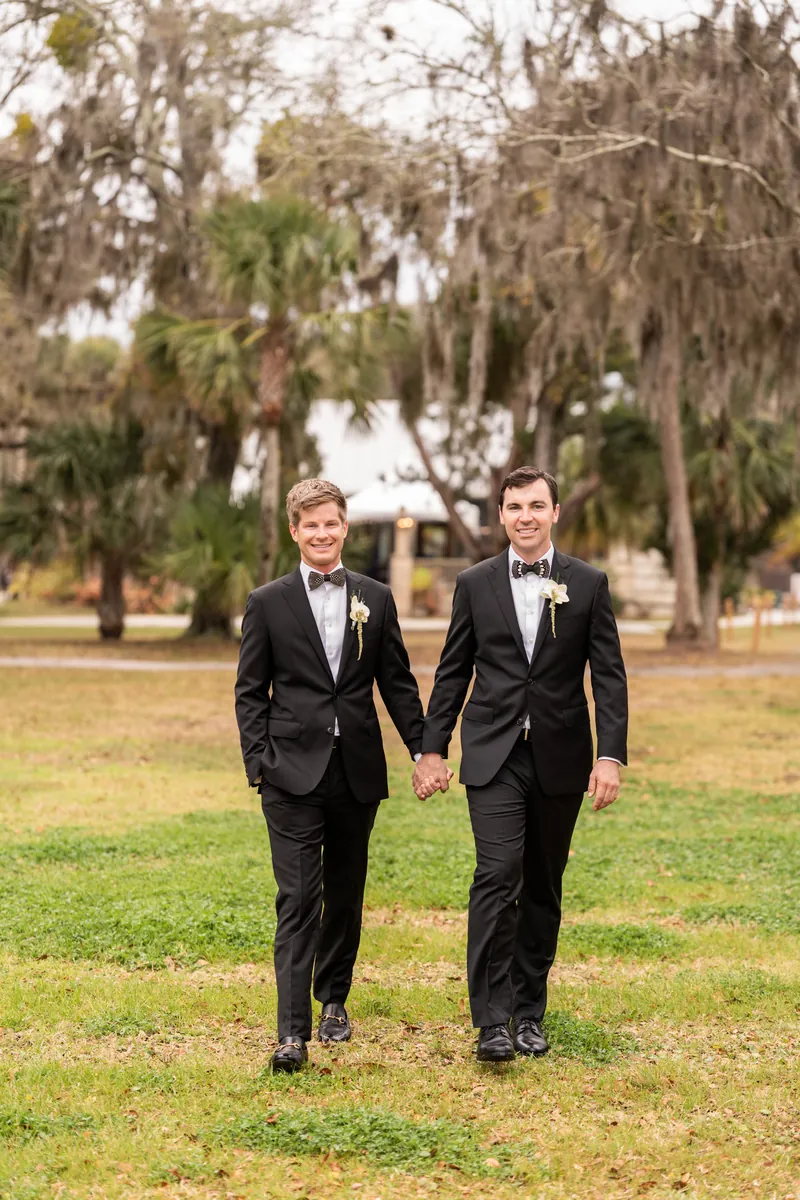 Kirkland and Austin face each other closely, both wearing black tuxedos with white boutonnières and bow ties.