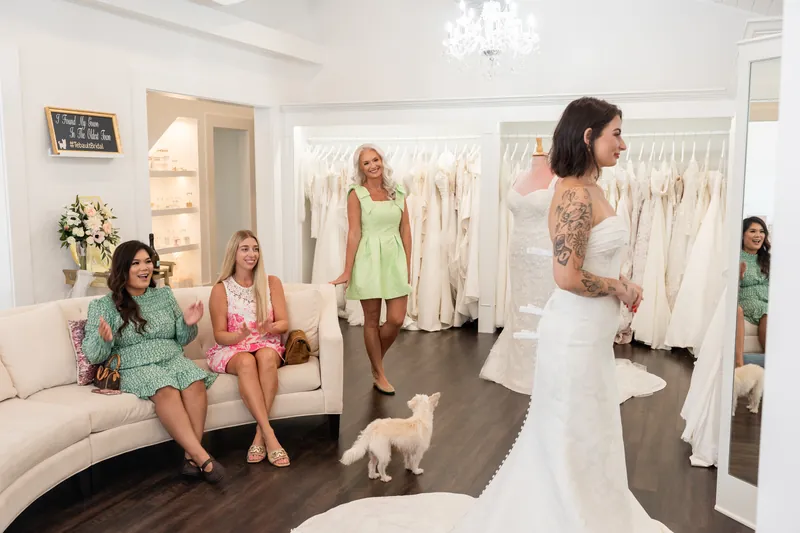 Guests seated on a cream sofa watch a bride in a white gown stand in the showroom at Tebault Bridal.