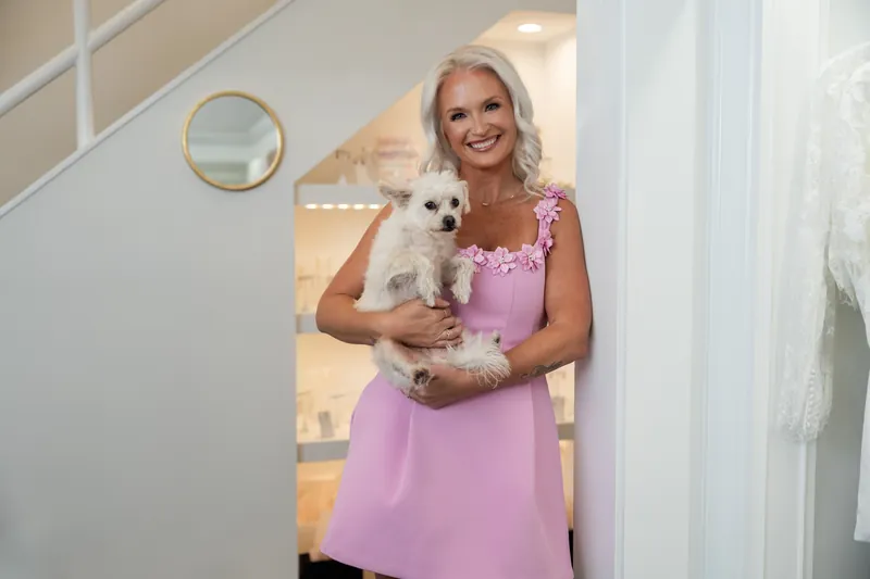 Kristen smiles while cradling a fluffy white puppy in her arms at the bridal boutique.
