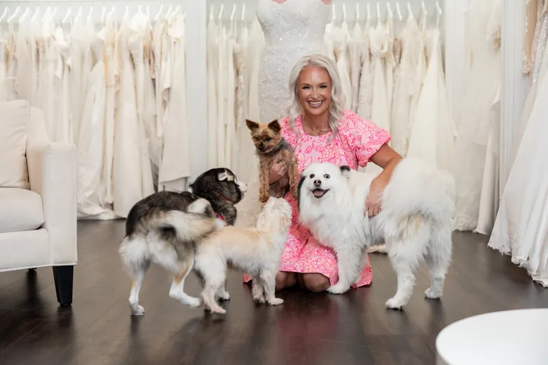 Kristen poses with four dogs of varying sizes on the dark floor, all wearing coordinated neutral and white tones.