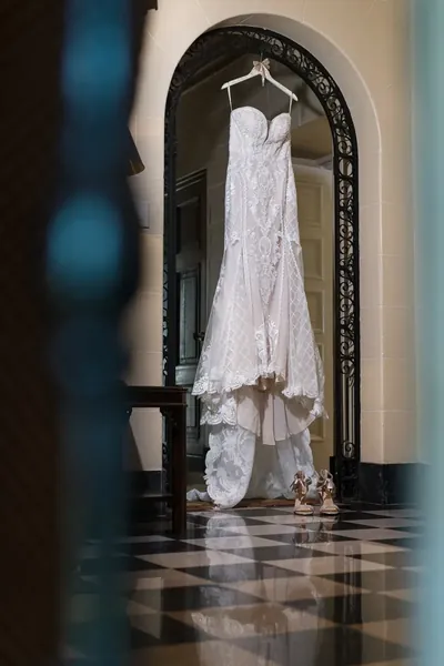 Elegant white lace wedding dress hanging in ornate archway with shoes below