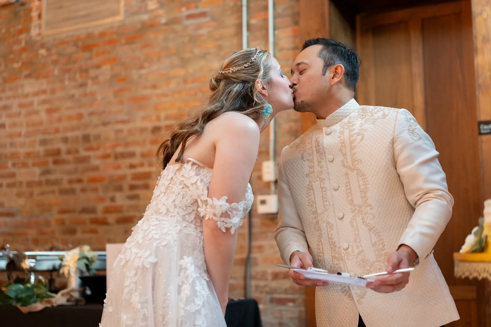 Couple kiss with exposed brick wall at Brick and Beam reception