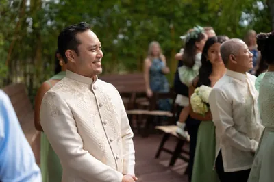 Groom Judd waiting at ceremony with family in Barong Tagalog bamboo backdrop