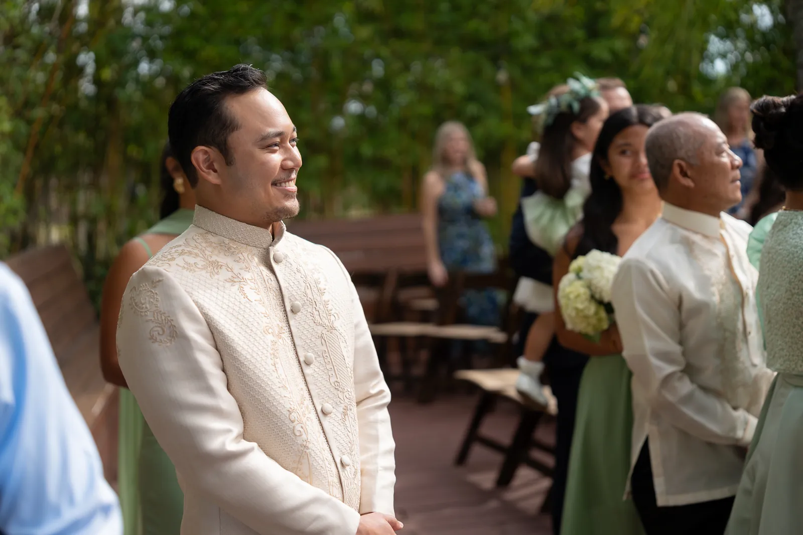 Groom Judd waiting at ceremony with family in Barong Tagalog bamboo backdrop