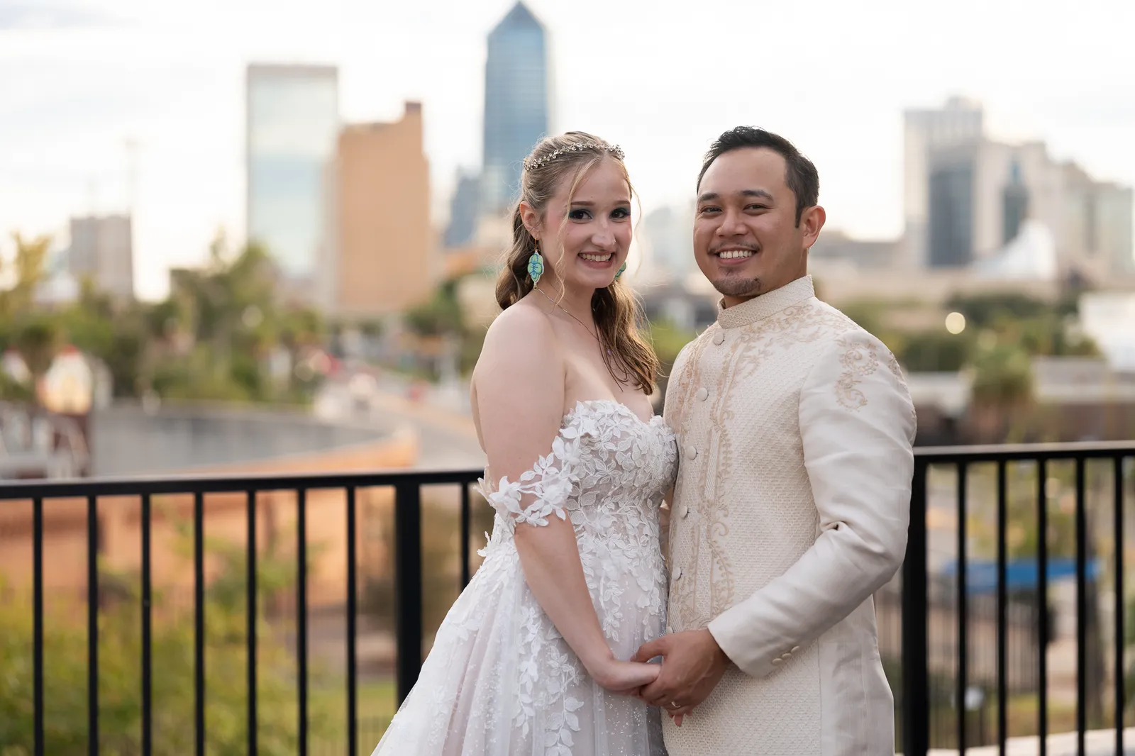 Couple in wedding attire posing before city skyline at sunset