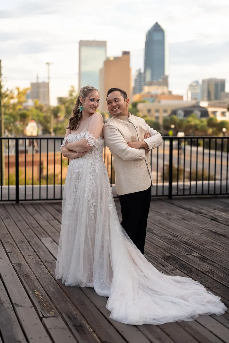 Kyra and Judd stand beneath a draped archway on a wooden deck, exchanging looks as guests watch from the foreground.