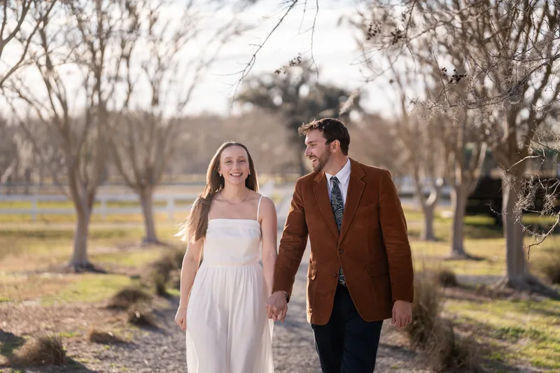 Lacey and Josh walking hand in hand down the tree-lined path at Congaree and Penn