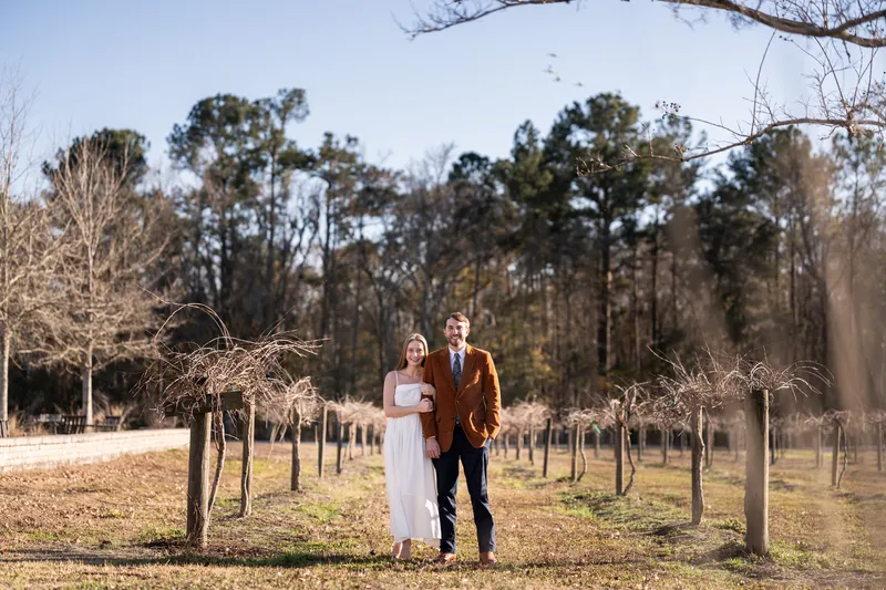 Lacey and Josh standing together among vineyard rows at Congaree and Penn