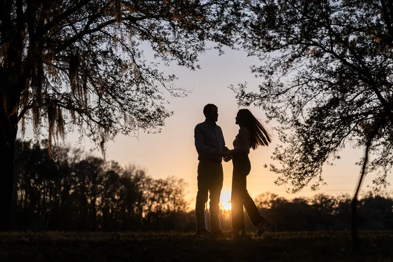 Silhouette of Lacey and Josh holding hands at sunset under the oaks