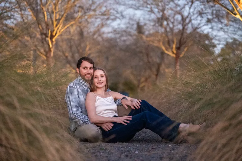 Lacey and Josh sitting on a gravel path surrounded by ornamental grasses at dusk