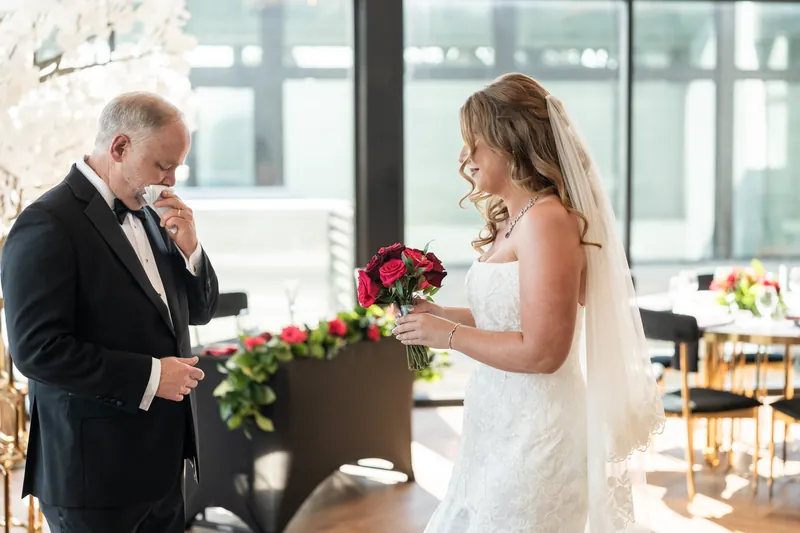 Kevin wipes away a tear while Lauren holds her bouquet during an emotional moment in the sunlit reception hall.