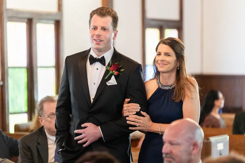 Kevin wears a black tuxedo with a pink boutonniere while walking arm-in-arm with Lauren down the aisle.