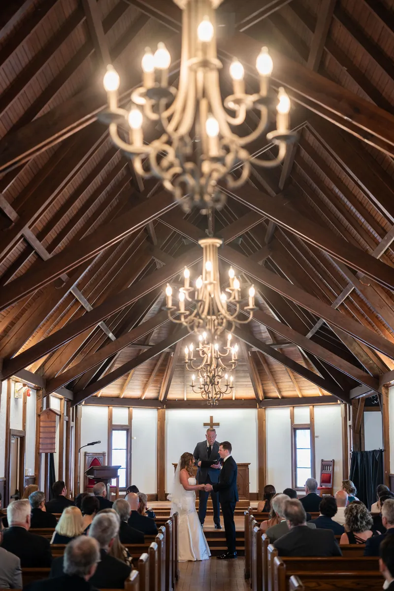 Wide-angle view of the wooden chapel with exposed beams and chandeliers during Lauren and Kevin's ceremony