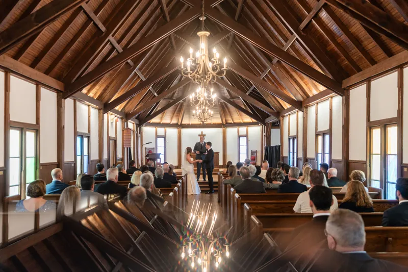 Chapel interior with vaulted wooden ceiling, chandeliers, and windows as guests watch Lauren and Kevin exchange vows