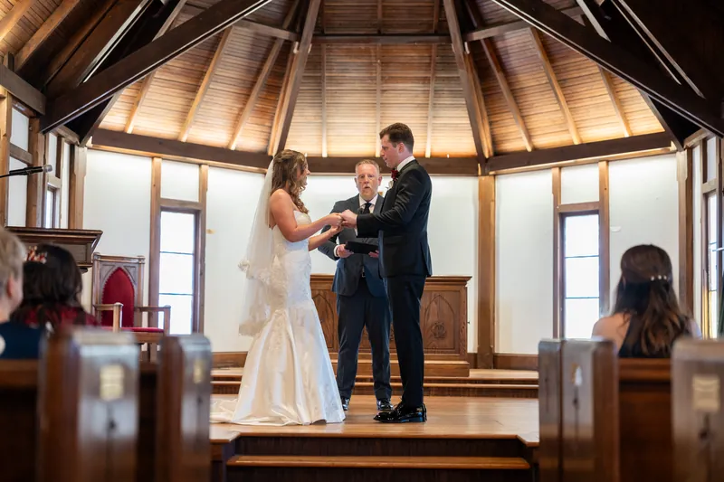 Kevin and Lauren face each other at the altar exchanging rings, with Kevin in a navy suit and Lauren in a white wedding gown.