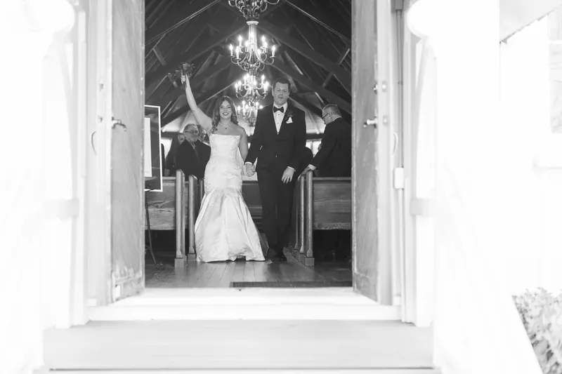 Lauren and Kevin stand at the altar inside a white chapel with crystal chandeliers, viewed through the open doorway.