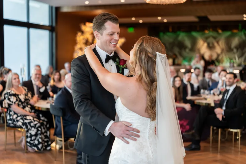 Kevin and Lauren share their first dance in a ballroom with guests seated at tables in the background.