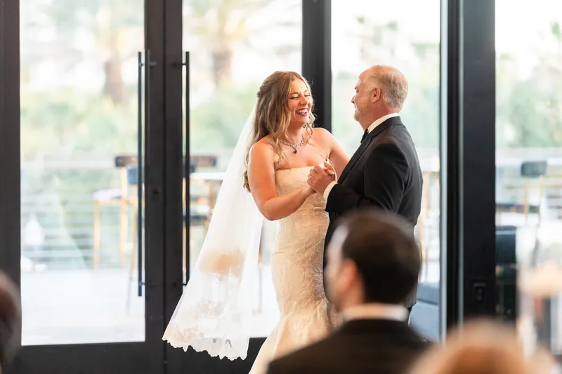 Lauren and Kevin face each other with hands clasped during their first dance at large windows with a city skyline view.