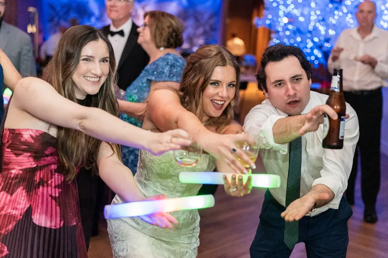 Three guests playing with glow sticks during the reception, laughing together while holding illuminated bracelets.
