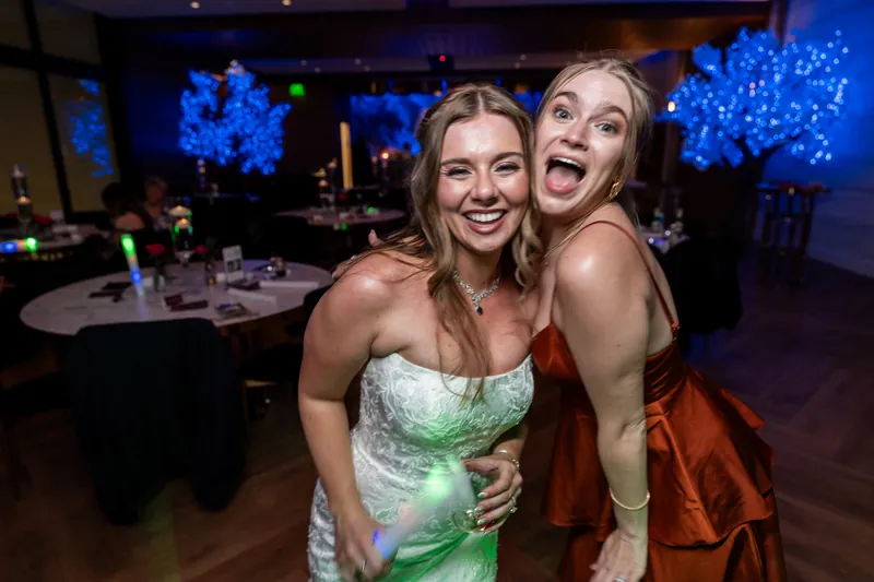 Two women posing for a photo at the reception, one wearing a green patterned dress and the other in an orange-red jacket.