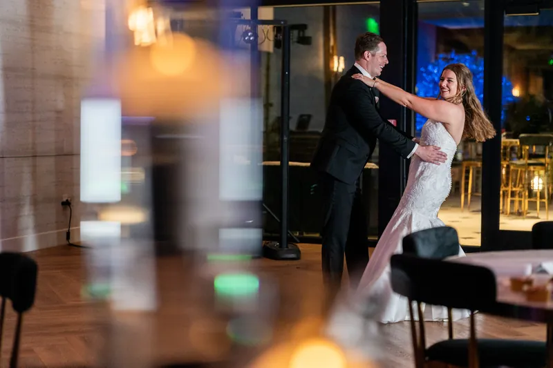Kevin spins Lauren across the dance floor at their first dance as blue and amber lighting illuminates the decorated venue.