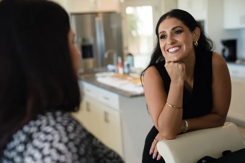Laurel smiles during a conversation in the bridal suite, resting her chin on her hand near a bathroom counter.