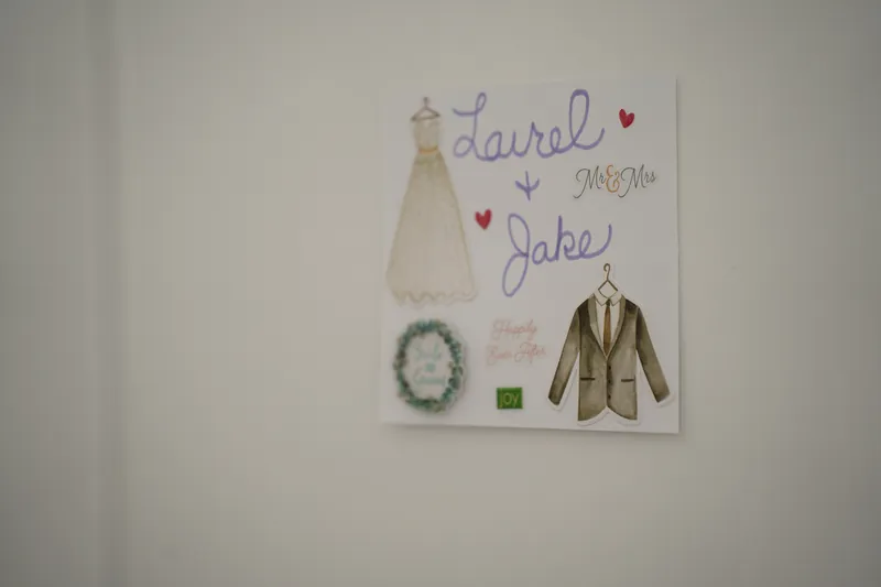 A custom illustration hangs on the wall showing Laurel and Jake's names with sketches of a wedding dress, suit, and florals.