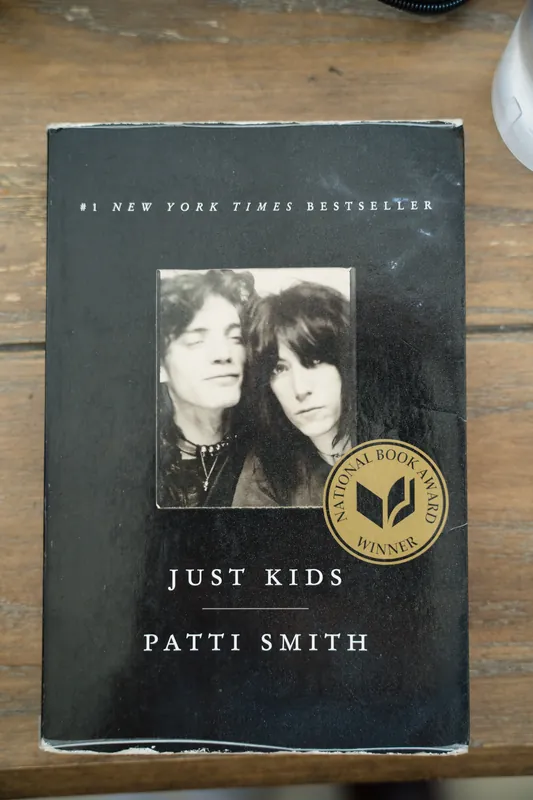 A copy of "Just Kids" by Patti Smith sits on a wooden floor, its black cover featuring a gold award seal.