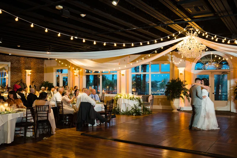 Laurel and Jake dance at The White Room as guests watch from round tables beneath string lights and a chandelier.