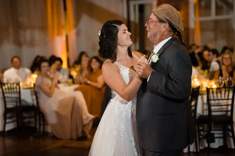 Laurel in a white wedding dress dances with her father as seated guests look on in the background.