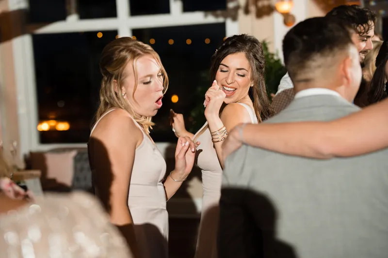 Two women laugh and chat at the reception, one touching her face while the other smiles broadly nearby.